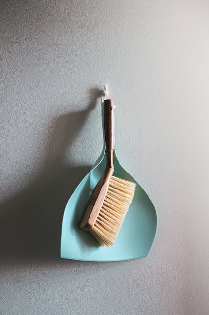 A team of three professional cleaners wearing matching dark uniforms are performing surface cleaning and deep cleaning in a modern, well-lit living room. The room features a large L-shaped sofa with a